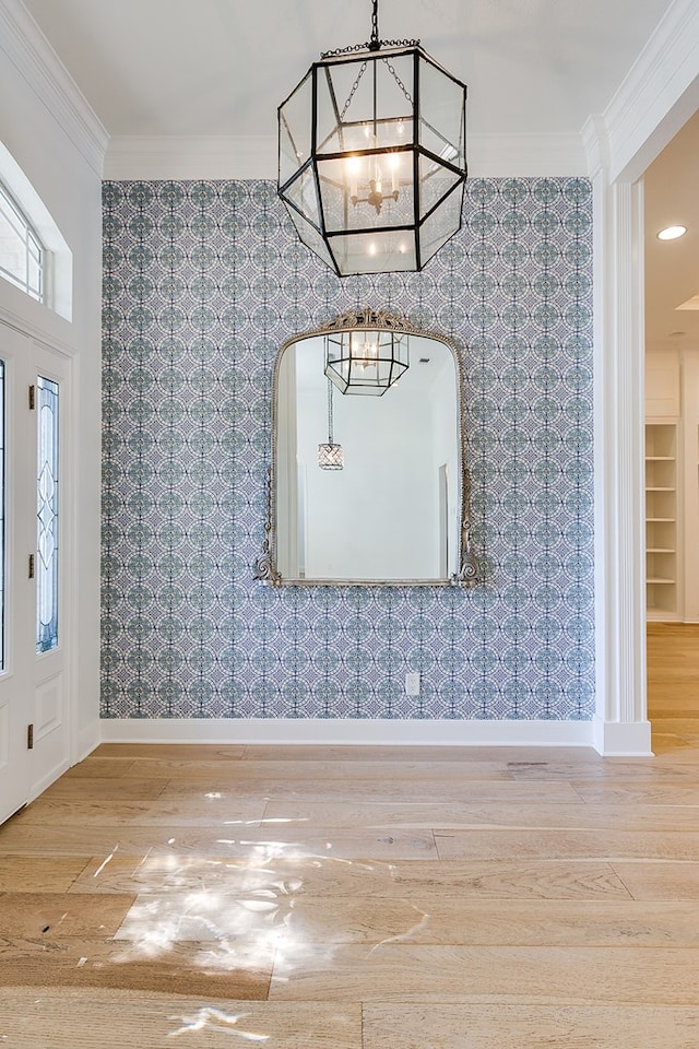 unfurnished dining area featuring an inviting chandelier, ornamental molding, wood finished floors, and wallpapered walls
