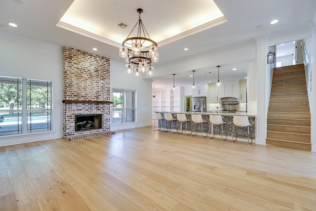 living area featuring crown molding, a chandelier, light wood-style floors, a tray ceiling, and visible vents