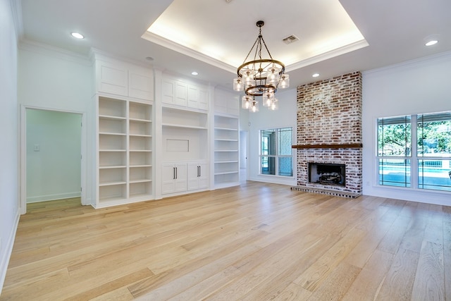 unfurnished living room featuring an inviting chandelier, ornamental molding, light wood-type flooring, and a raised ceiling