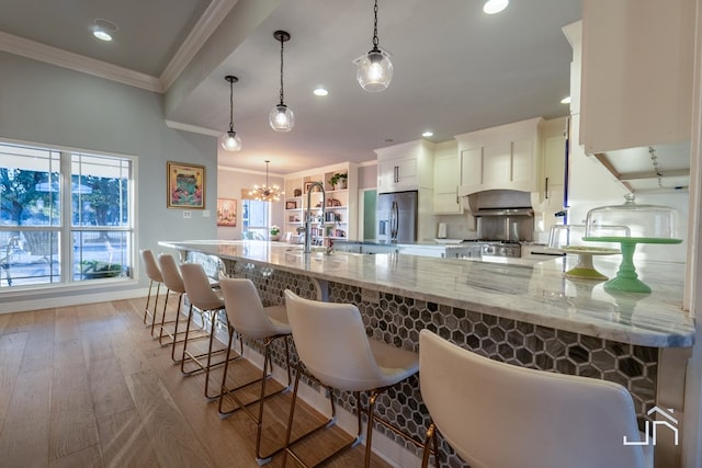 kitchen with stainless steel fridge, a breakfast bar, white cabinetry, hanging light fixtures, and light stone counters