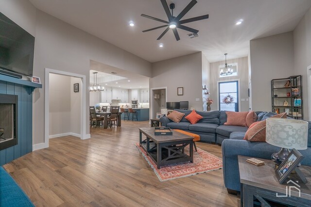living area with a towering ceiling, visible vents, ceiling fan with notable chandelier, and wood finished floors