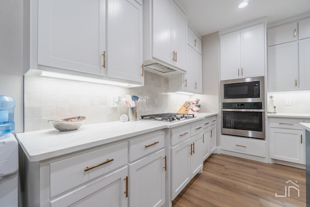 kitchen featuring tasteful backsplash, appliances with stainless steel finishes, light wood finished floors, and white cabinetry