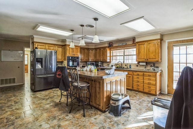 kitchen featuring crown molding, black oven, hanging light fixtures, a center island, and stainless steel fridge with ice dispenser