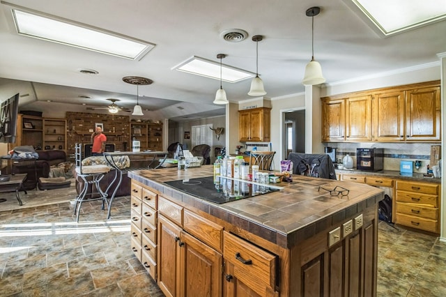 kitchen featuring hanging light fixtures, black electric stovetop, tile counters, ornamental molding, and a kitchen island