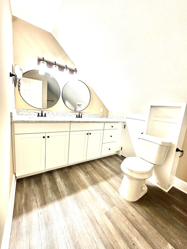 bathroom featuring wood-type flooring, lofted ceiling, vanity, and toilet