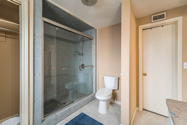 bathroom featuring toilet, a shower with shower door, and tile patterned flooring