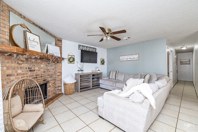 living room featuring light tile patterned floors, ceiling fan, a textured ceiling, and a brick fireplace