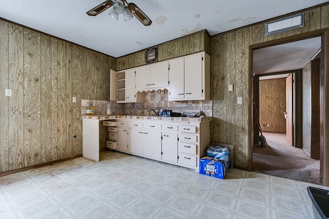 kitchen with wood walls, light carpet, a textured ceiling, and white cabinets