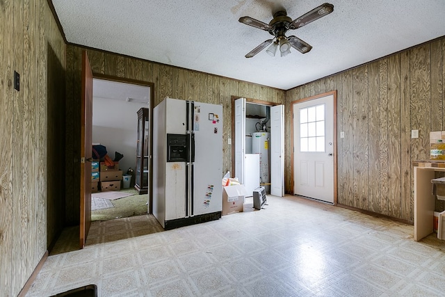 interior space with a textured ceiling, gas water heater, ceiling fan, and wood walls