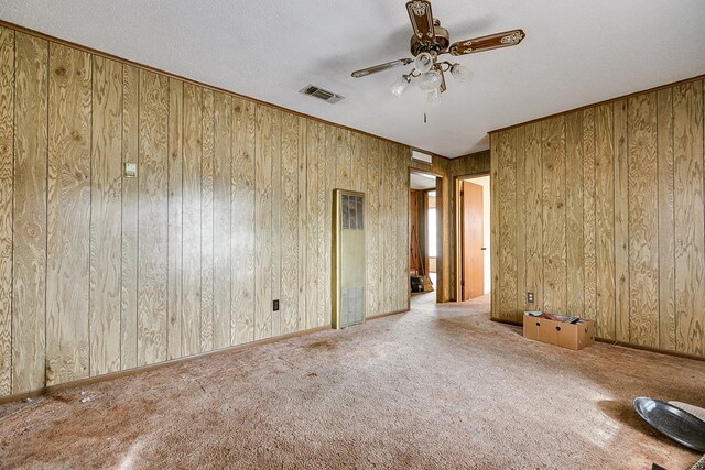 carpeted spare room with a textured ceiling, ceiling fan, and wood walls