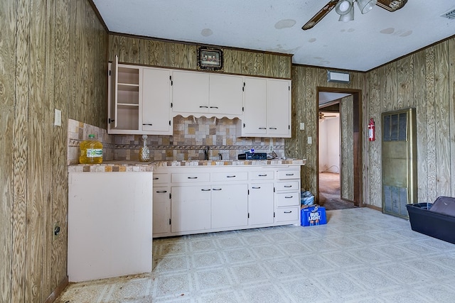 kitchen featuring wood walls, sink, white cabinets, ceiling fan, and a textured ceiling