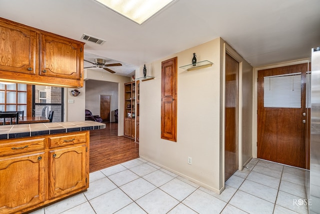 1729 Parkview Dr, San Angelo, TX 76904 - kitchen featuring tile counters, brown cabinetry, light tile patterned floors, and a ceiling fan