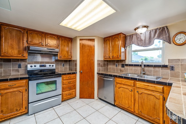 1729 Parkview Dr, San Angelo, TX 76904 - kitchen featuring stainless steel appliances, under cabinet range hood, tile counters, brown cabinets, and backsplash