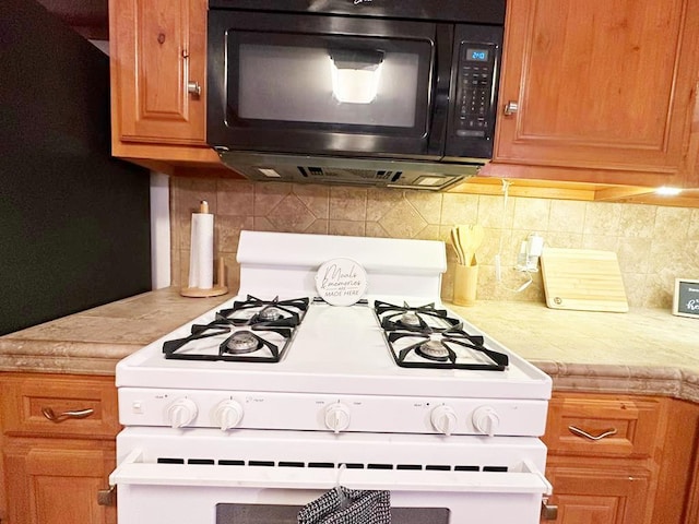 kitchen featuring black microwave, light countertops, white gas range oven, and backsplash