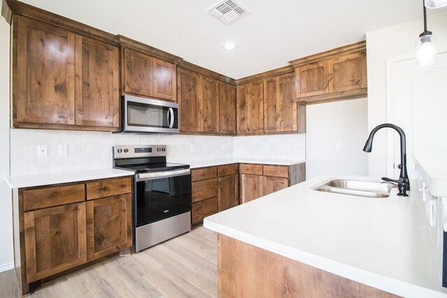 kitchen featuring sink, light wood-type flooring, pendant lighting, stainless steel appliances, and backsplash