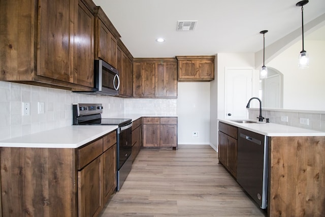 kitchen with tasteful backsplash, sink, hanging light fixtures, stainless steel appliances, and light wood-type flooring