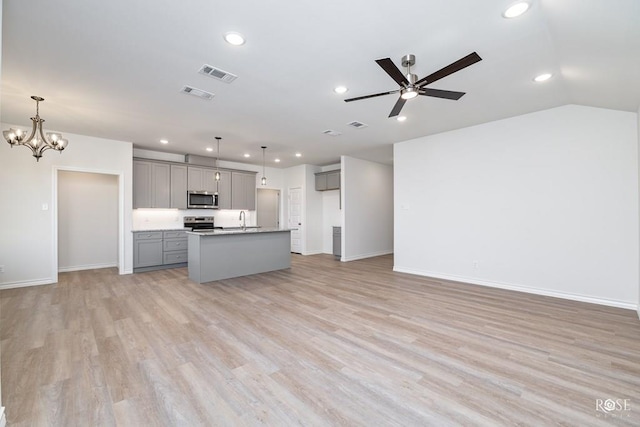 kitchen with sink, appliances with stainless steel finishes, gray cabinetry, a kitchen island with sink, and decorative light fixtures