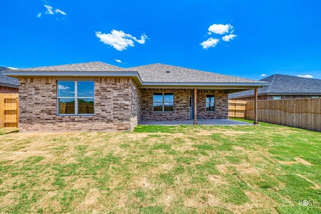 back of house featuring a patio, brick siding, fence, a yard, and roof with shingles