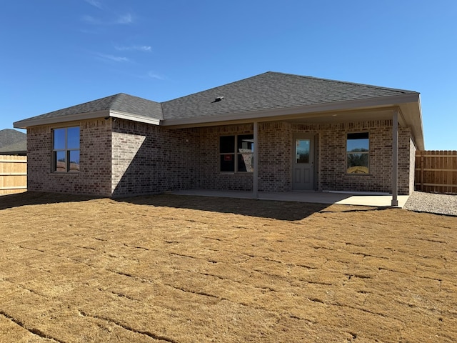 rear view of property featuring a patio, brick siding, a shingled roof, and fence