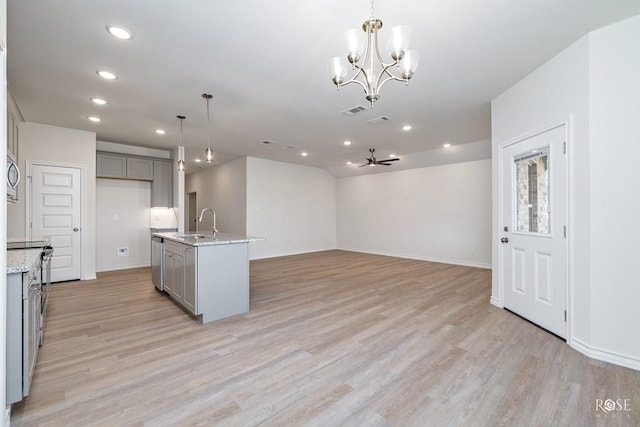 kitchen featuring gray cabinets, pendant lighting, stainless steel appliances, light stone countertops, and a kitchen island with sink