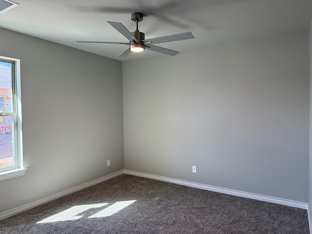 spare room with plenty of natural light, visible vents, dark colored carpet, and baseboards