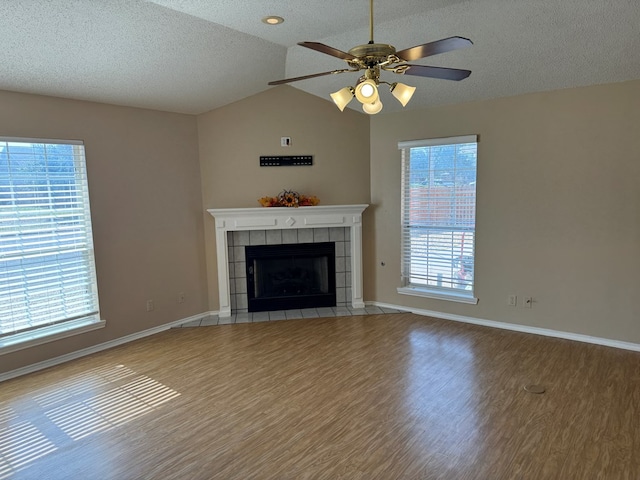 unfurnished living room featuring lofted ceiling, plenty of natural light, a tiled fireplace, and hardwood / wood-style floors