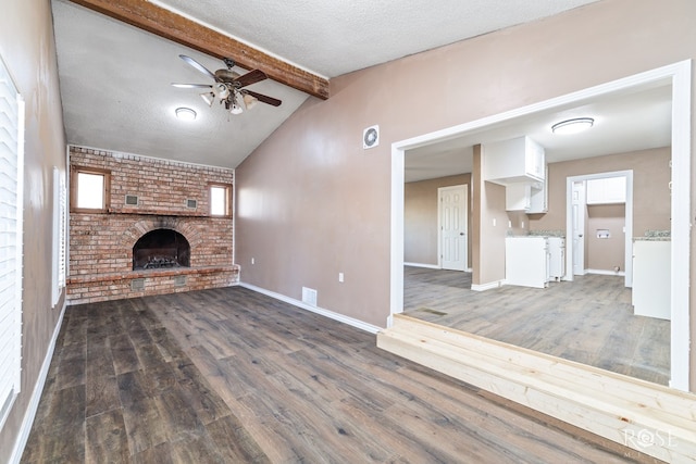 unfurnished living room with a fireplace, vaulted ceiling with beams, dark hardwood / wood-style flooring, ceiling fan, and a textured ceiling