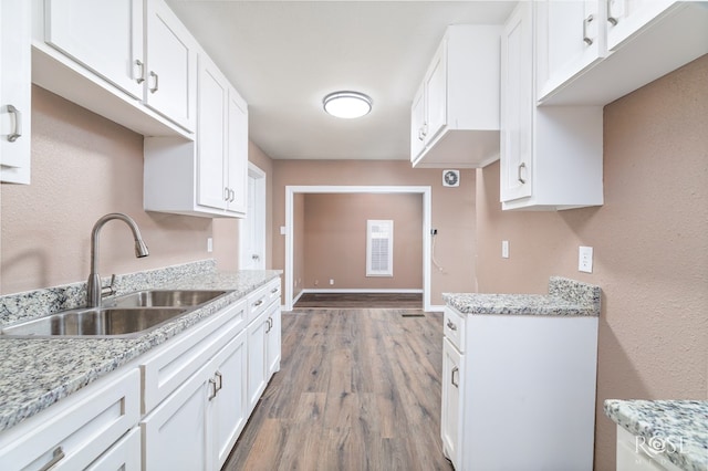 kitchen with hardwood / wood-style flooring, light stone countertops, sink, and white cabinets