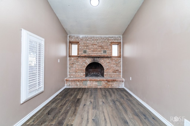 unfurnished living room with dark hardwood / wood-style floors, lofted ceiling, a fireplace, and a textured ceiling