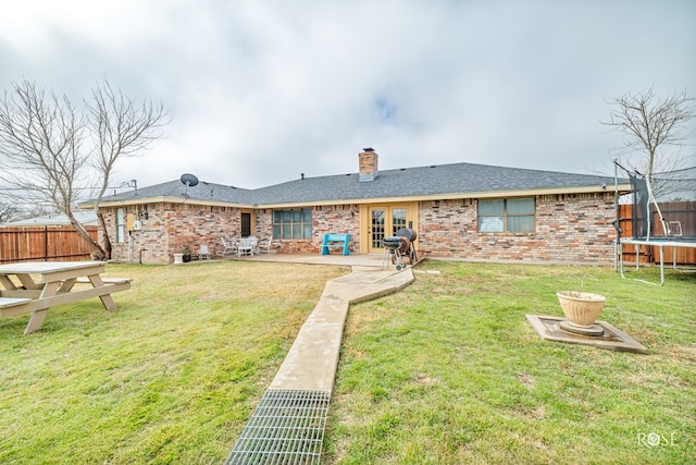 rear view of house with french doors, a patio, a trampoline, and a lawn