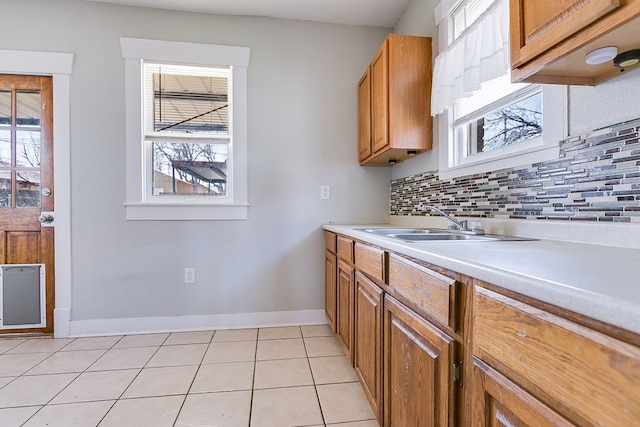 kitchen featuring tasteful backsplash, light countertops, light tile patterned floors, brown cabinetry, and a sink