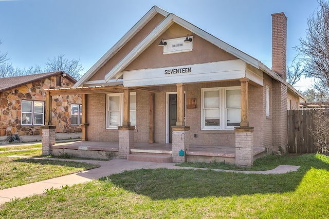 bungalow with brick siding, a front lawn, fence, covered porch, and a chimney