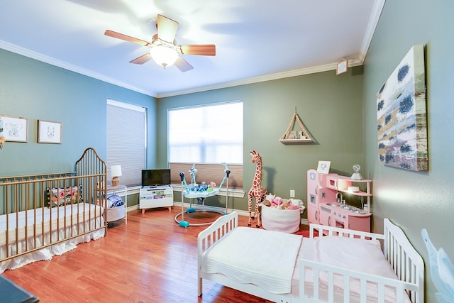 bedroom featuring hardwood / wood-style flooring, ornamental molding, a nursery area, and ceiling fan