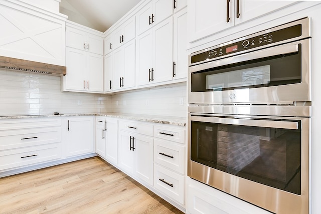 kitchen featuring backsplash, white cabinets, light stone counters, stainless steel double oven, and light wood-type flooring