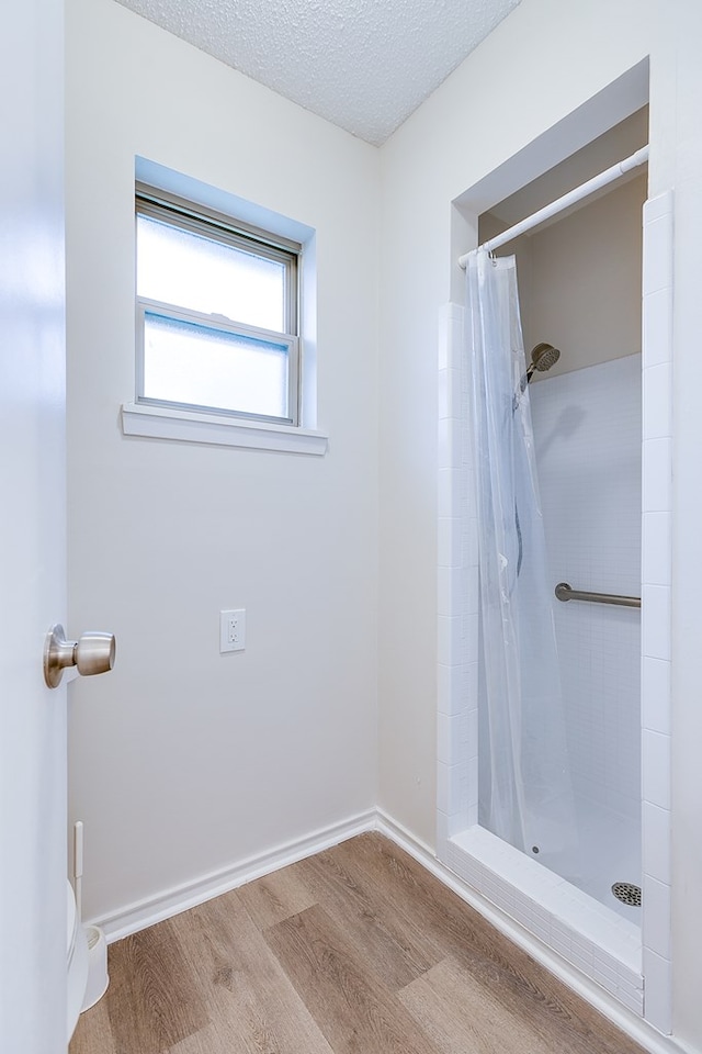 1809 N Harrison St, San Angelo, TX 76901 - bathroom featuring toilet, wood finished floors, a textured ceiling, baseboards, and a tile shower