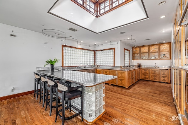 1703 Christoval Rd, San Angelo, TX 76903 - kitchen with stainless steel counters, brown cabinetry, a peninsula, a breakfast bar area, and light wood-style floors