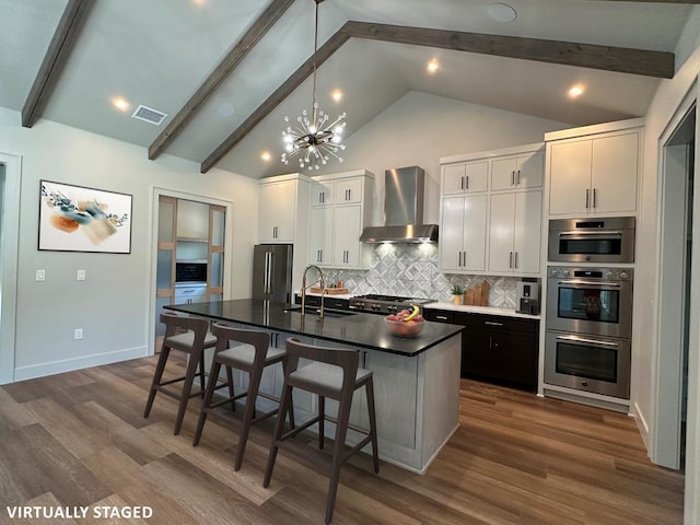 1603 Paseo De Vaca St, San Angelo, TX 76901 - kitchen featuring wall chimney range hood, a chandelier, beamed ceiling, a kitchen island with sink, and decorative backsplash