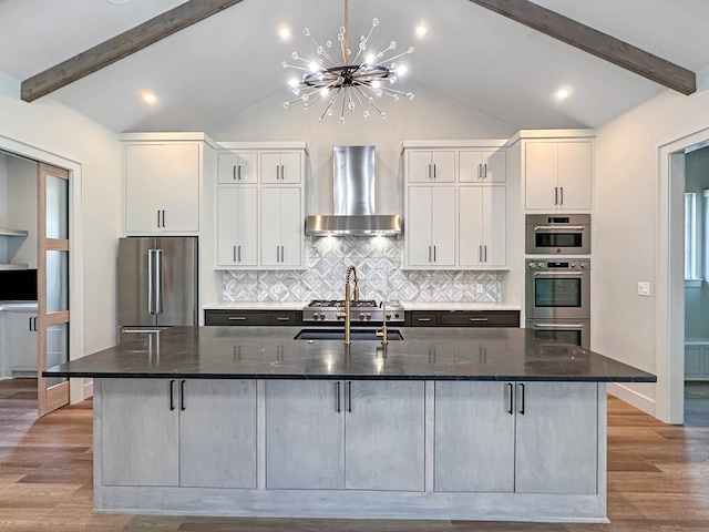 1603 Paseo De Vaca St, San Angelo, TX 76901 - kitchen with wall chimney range hood, appliances with stainless steel finishes, a kitchen island with sink, decorative backsplash, and white cabinets