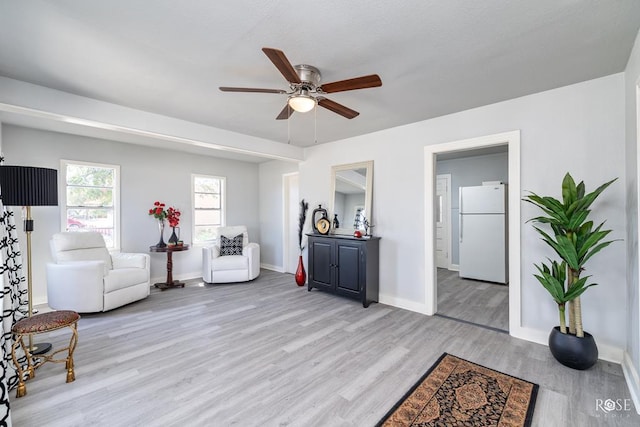living area featuring baseboards, a ceiling fan, and light wood finished floors