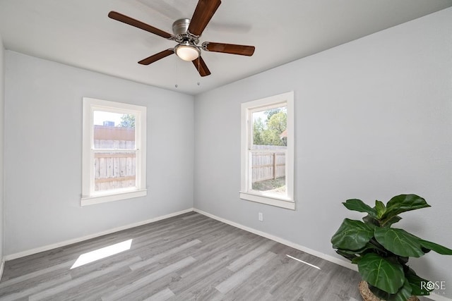 empty room featuring baseboards, a ceiling fan, wood finished floors, and a wealth of natural light