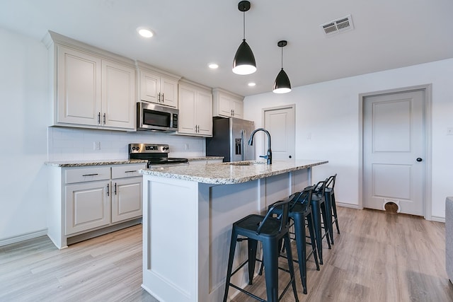 1501 Montague Ave, San Angelo, TX 76905 - kitchen with stainless steel appliances, light wood-style floors, backsplash, an island with sink, and a kitchen bar