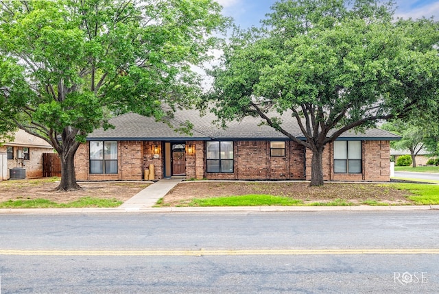 single story home featuring central AC unit, roof with shingles, and brick siding