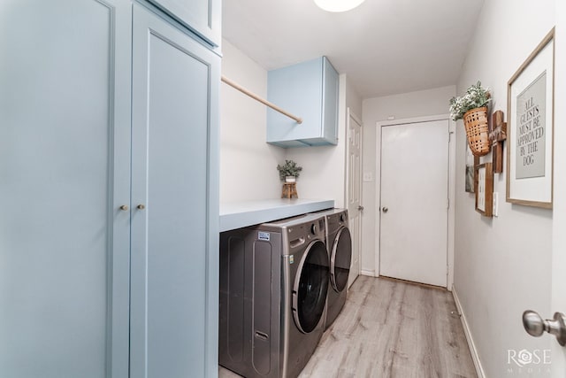 clothes washing area featuring cabinet space, light wood-style floors, washing machine and clothes dryer, and baseboards