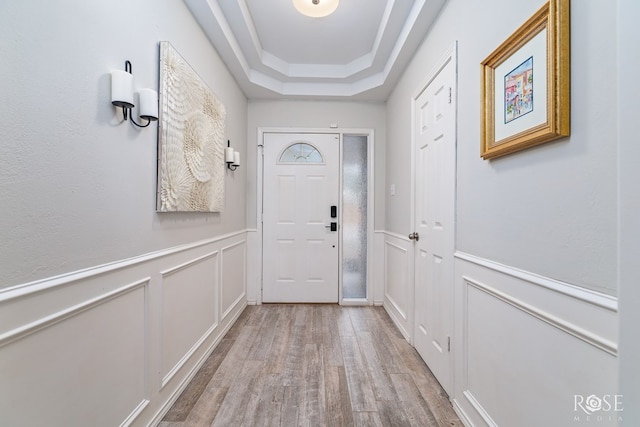 doorway with wood finished floors, a decorative wall, a raised ceiling, and wainscoting