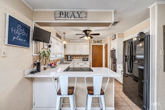 2029 China St, Brady, TX 76825 - kitchen with black appliances, a peninsula, a textured ceiling, a ceiling fan, and a kitchen bar