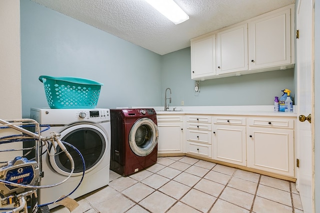 clothes washing area with sink, cabinets, light tile patterned floors, washing machine and clothes dryer, and a textured ceiling