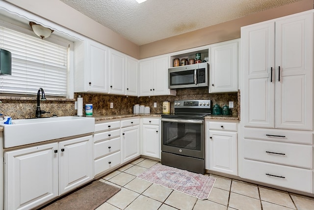 kitchen with sink, light tile patterned floors, appliances with stainless steel finishes, white cabinetry, and a textured ceiling