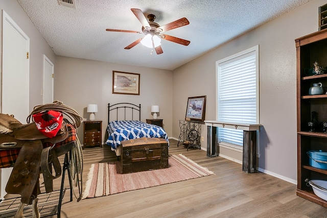 bedroom with multiple windows, light wood-type flooring, a textured ceiling, and ceiling fan