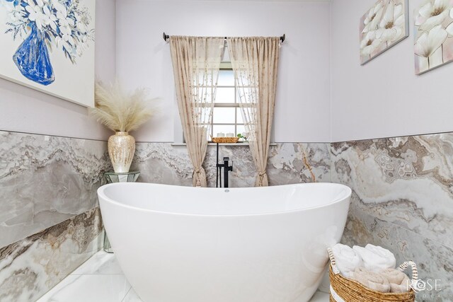 full bathroom with tile walls, a soaking tub, a wainscoted wall, and marble finish floor