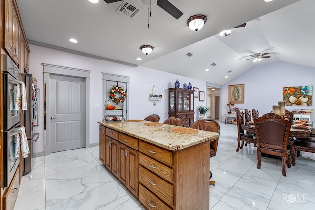 kitchen featuring lofted ceiling, light stone counters, a kitchen breakfast bar, a kitchen island, and ceiling fan